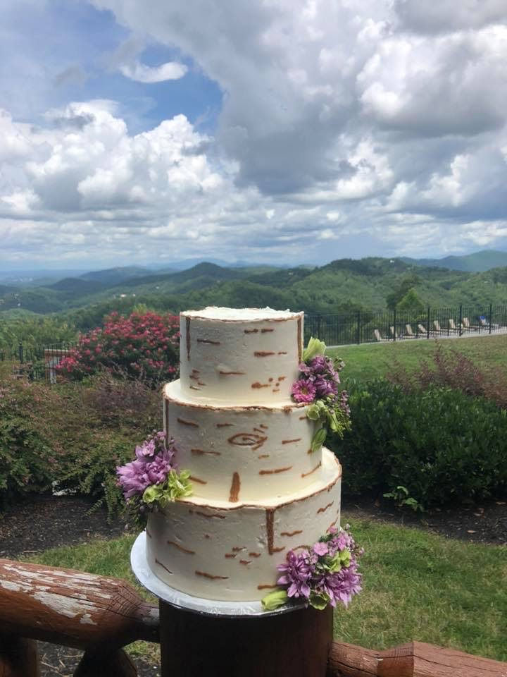 Three-tiered wedding cake with floral decorations against a scenic mountain backdrop