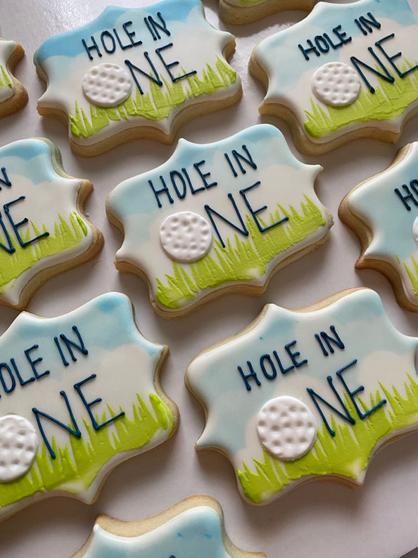 Decorative cookies with 'Hole in One' text and golf ball design on a white surface