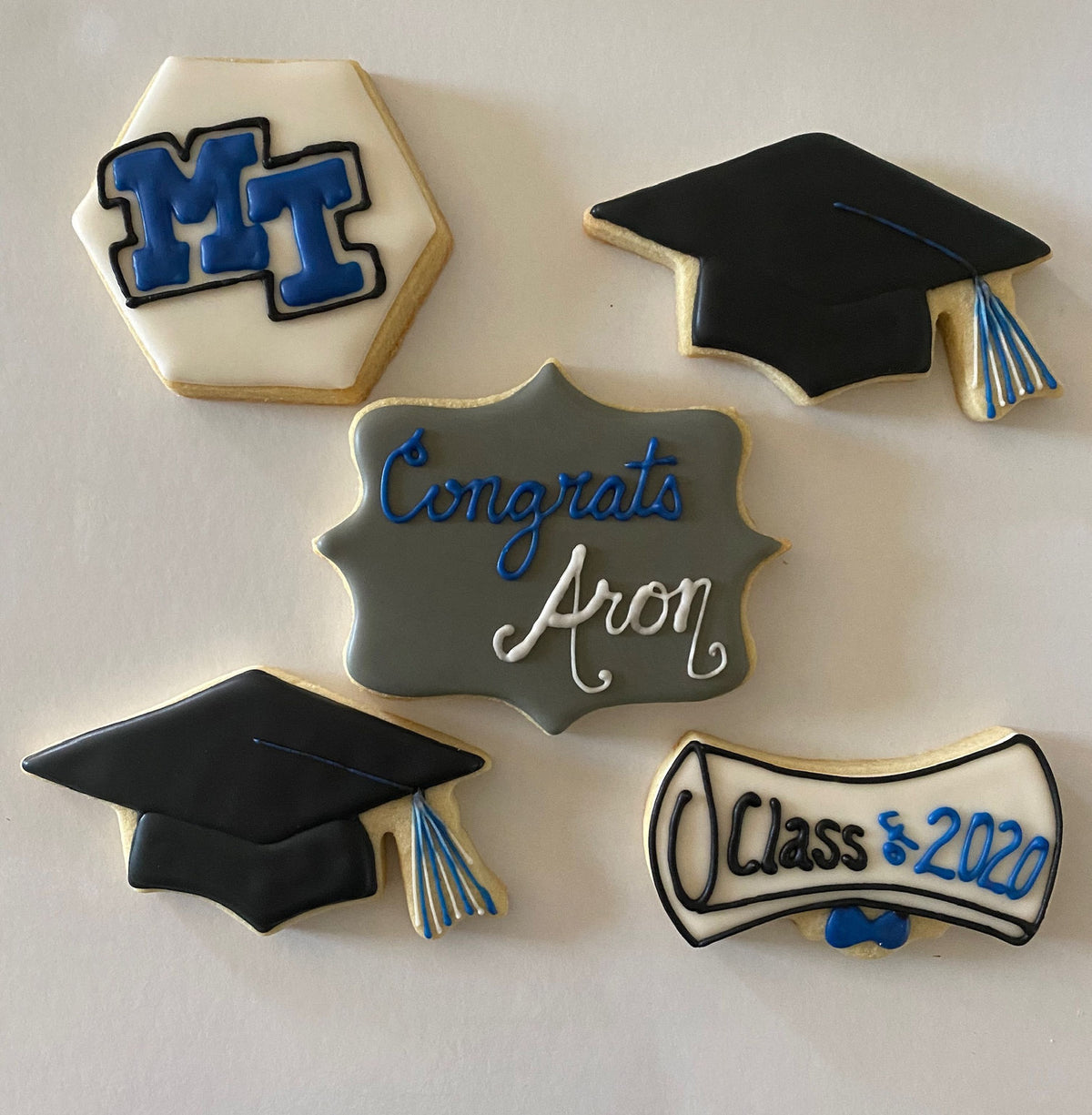 Decorative cookies shaped like a graduation cap, diploma, and 'Congrats Aron' sign on a white background.